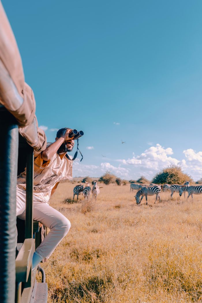Mastering the First Impression: Your intriguing post title goes here A man enjoys a wildlife safari in Nairobi, Kenya, observing zebras through binoculars from a truck.