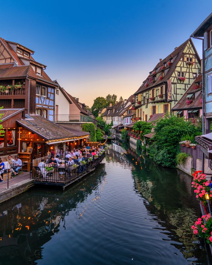 Menu Scenic view of a picturesque canal with half-timbered houses in Colmar during sunset.