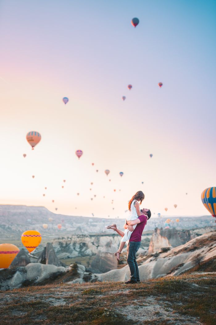 Menu A couple shares a romantic moment at sunrise with hot air balloons in Cappadocia, Turkey.