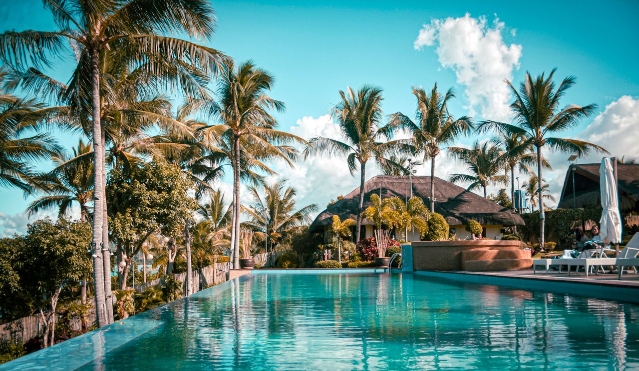 Menu Scenic view of a luxury tropical resort with palm trees and an inviting pool.